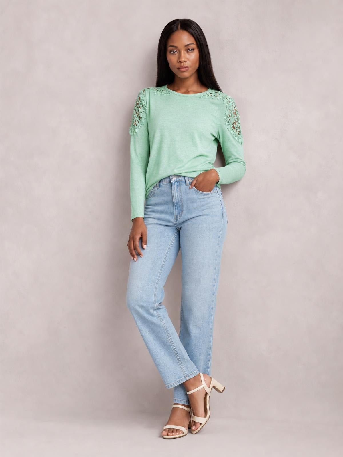 Model wears a mint green cutout round neck long sleeve T-shirt with floral lace detail at the shoulders, relaxed silhouette, and one hand in her pocket.