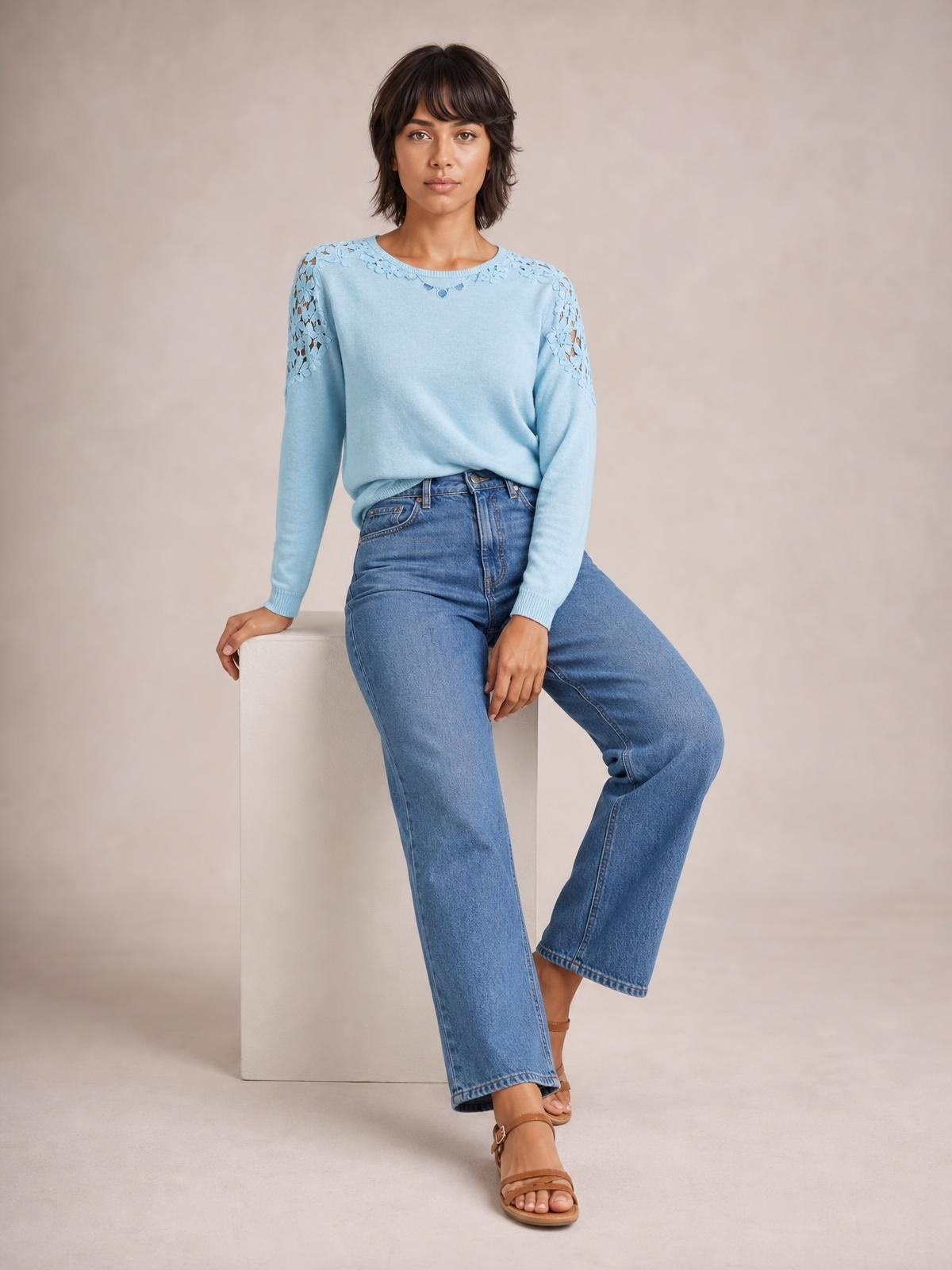 Model seated in a light blue cutout round neck long sleeve T-shirt with lace detailing at the neckline and shoulders and a relaxed silhouette.