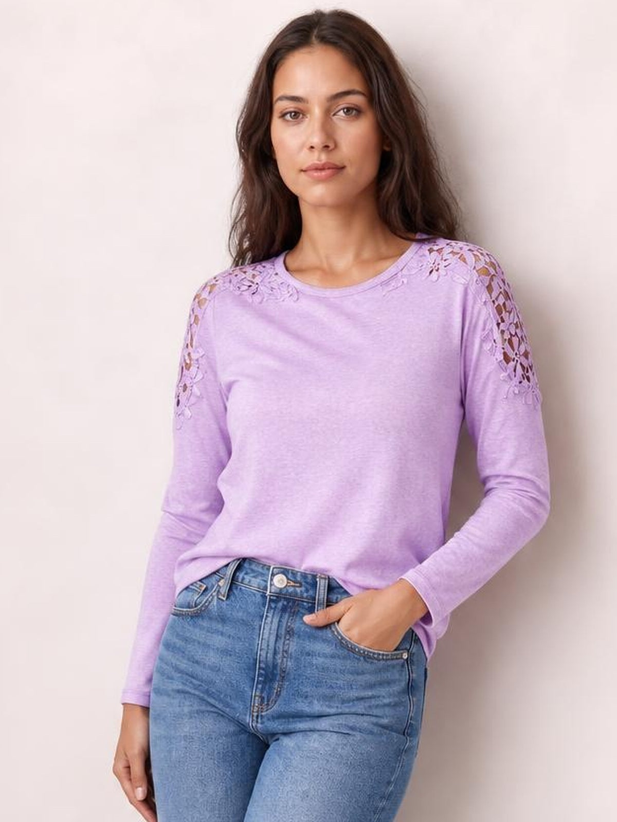 Model wearing a lavender cutout round neck long sleeve T-shirt with floral lace details along the shoulders and sleeves, shown in a relaxed fit with one hand in her jeans pocket.