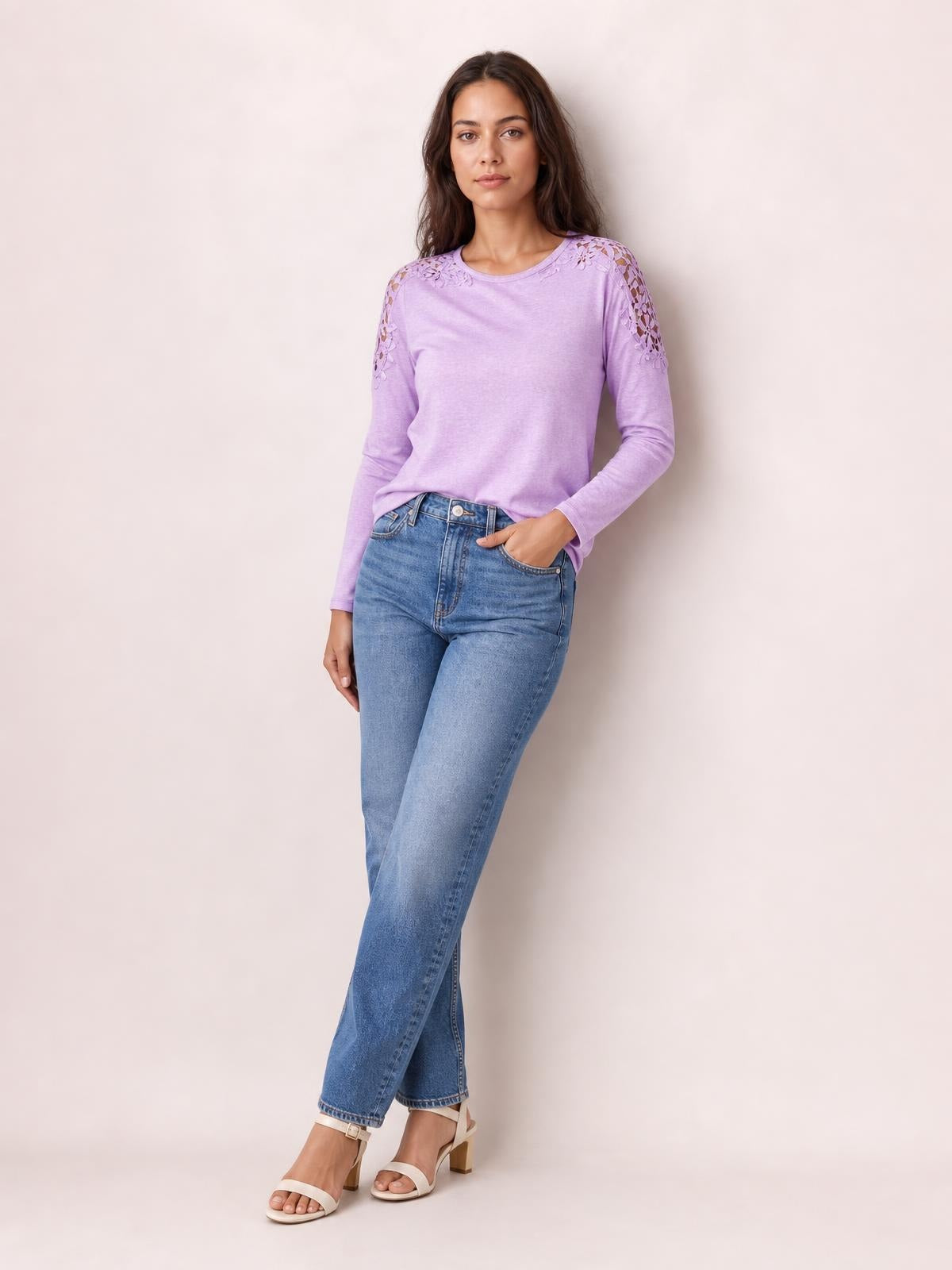 A model poses in a lavender cutout round neck long sleeve T-shirt with lace shoulder details, a relaxed silhouette, and one hand in her jeans pocket.