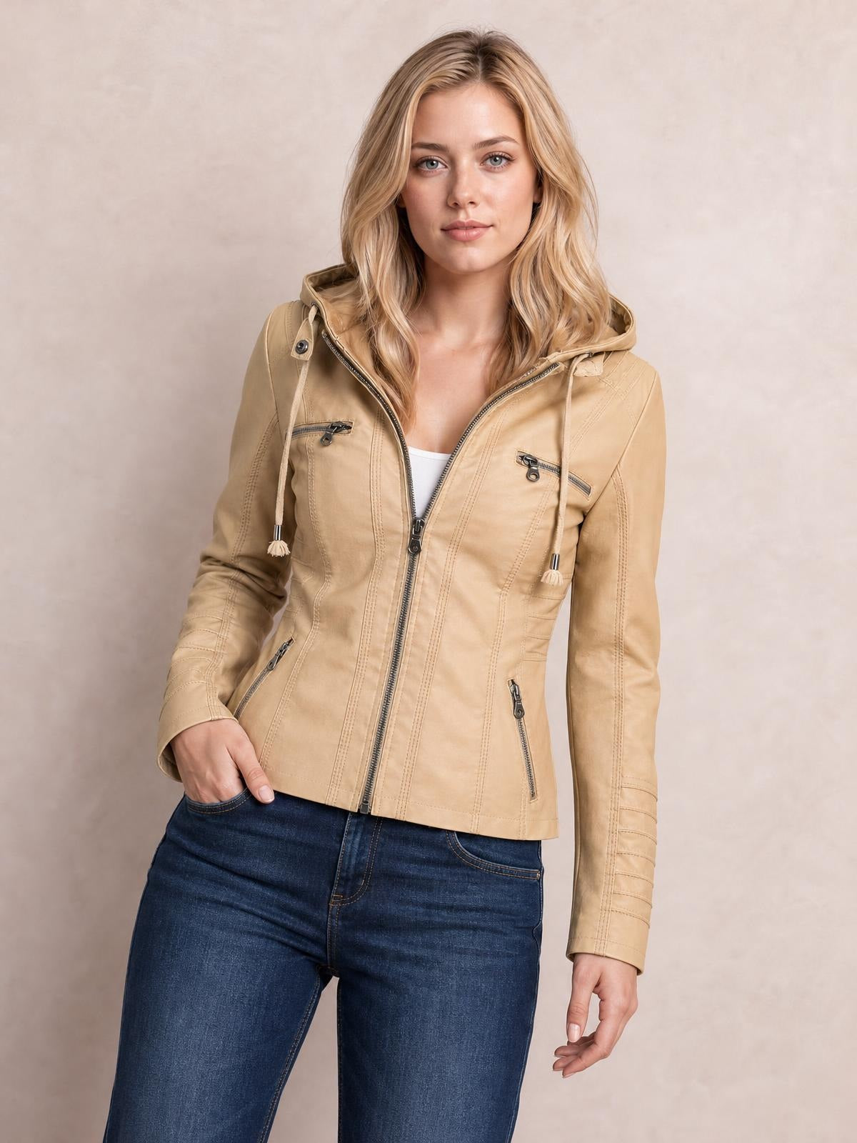 Model poses in a tan faux leather moto jacket with a hood, drawstrings, zip closure, seam detailing, and multiple zippered pockets.