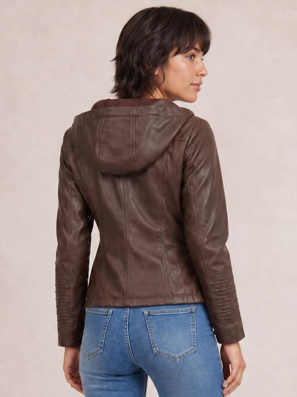 Model shown from the back in a brown faux leather moto jacket with a hood, long sleeves, vertical seam detailing, and a regular fit, looking over her shoulder.