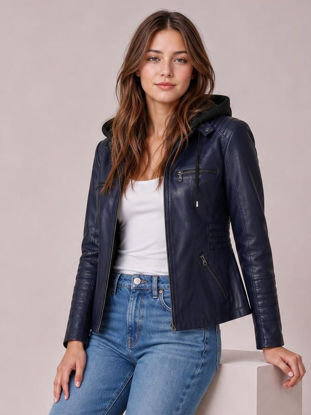 Model wearing a navy faux leather moto jacket with hood, zip closure, seam detailing, zippered pockets, and a regular fitted silhouette.