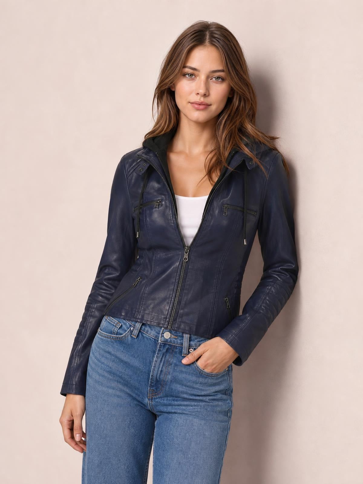 Model poses in a navy faux leather moto jacket with a zip front, hood, seam detailing, and multiple zippered pockets in a regular silhouette.
