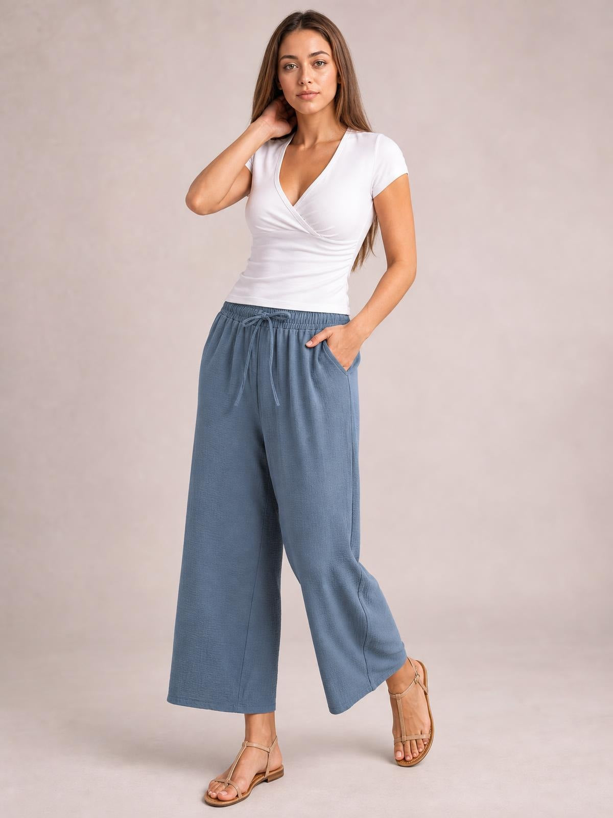 Model poses in blue-gray cropped jogger pants with a drawstring waist, elastic waistband, roomy straight-leg silhouette, and side pockets.