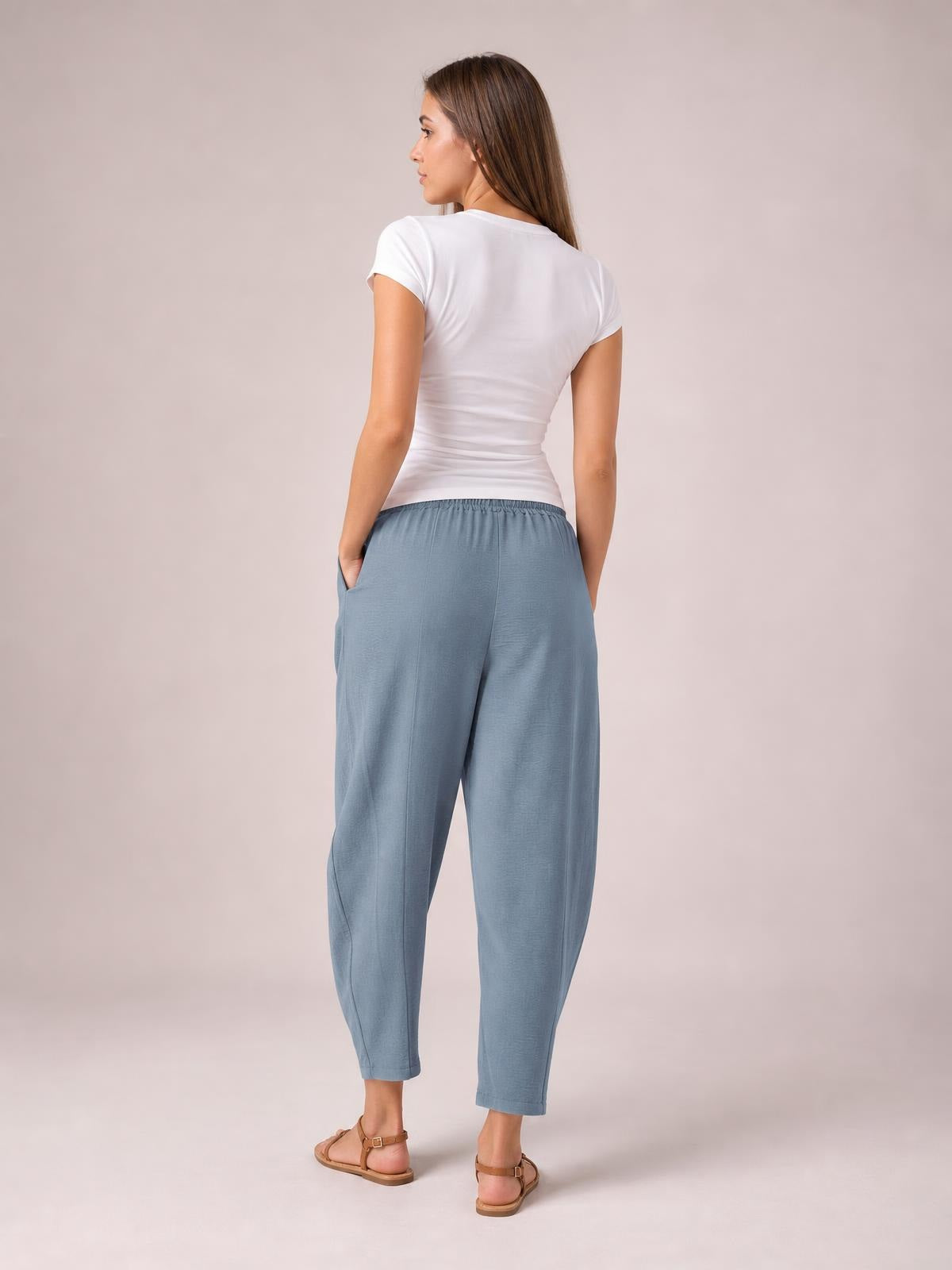 A model is shown from behind wearing blue-gray drawstring cropped jogger pants with an elastic waistband, side pockets, and a relaxed tapered silhouette.