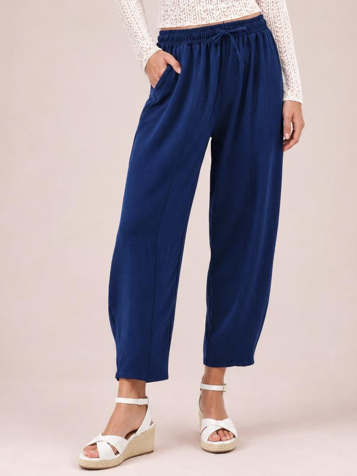 A model poses in navy cropped jogger pants with a relaxed wide-leg silhouette, elastic drawstring waist, and side pockets, with one hand tucked inside.