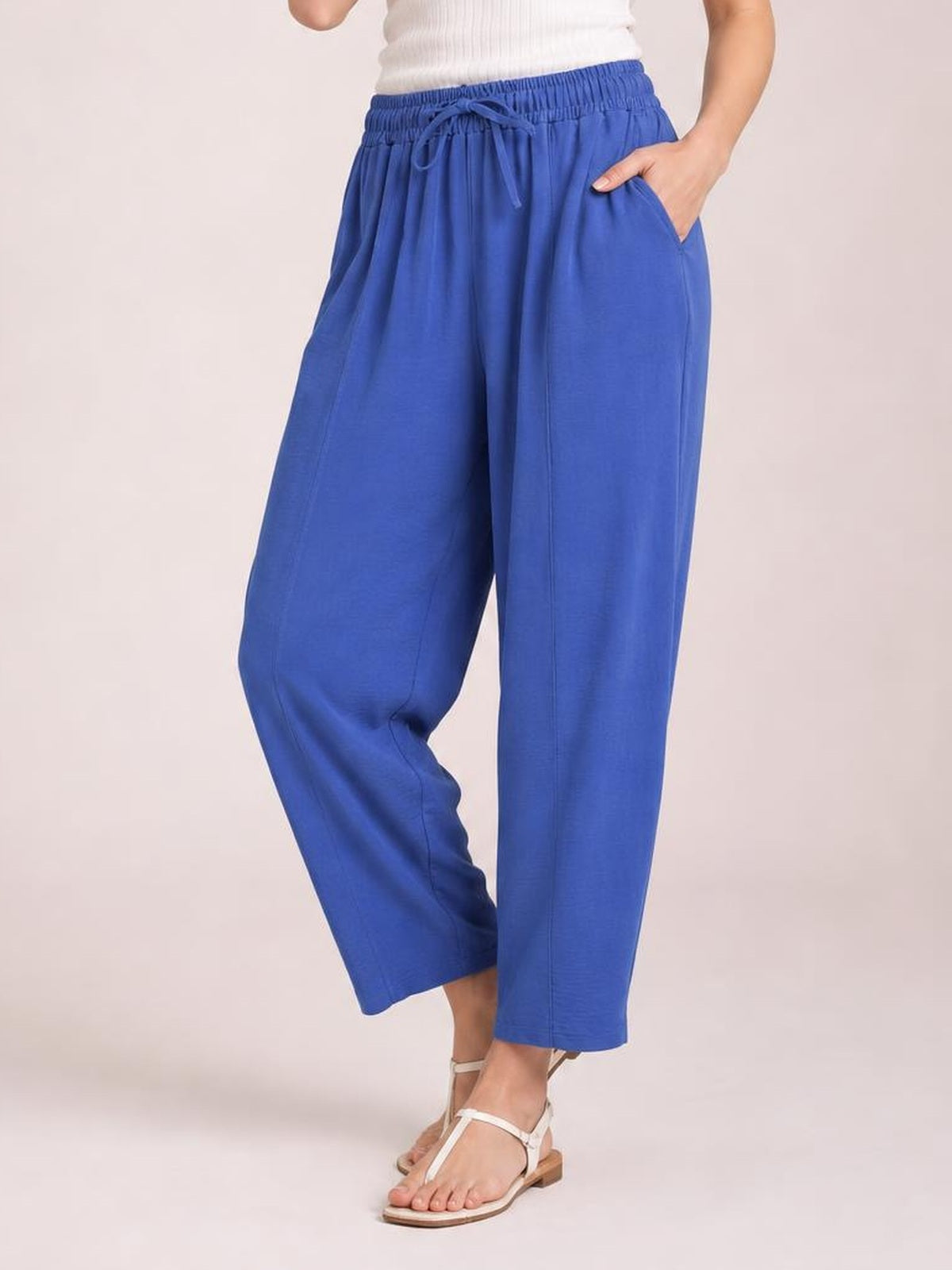 A model wears bright blue cropped jogger pants with a wide-leg silhouette, elastic drawstring waist, side pockets, and one bent leg.