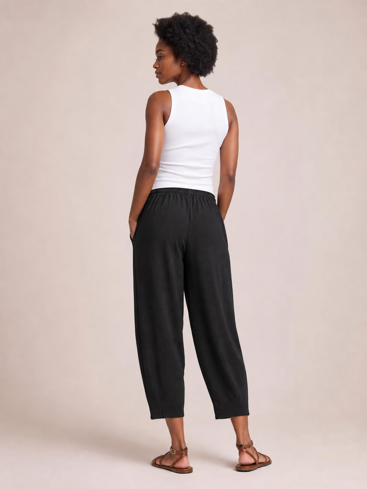 A model poses in black drawstring cropped jogger pants with an elastic waist, relaxed wide-leg silhouette, side pockets, and ankle-length hems.