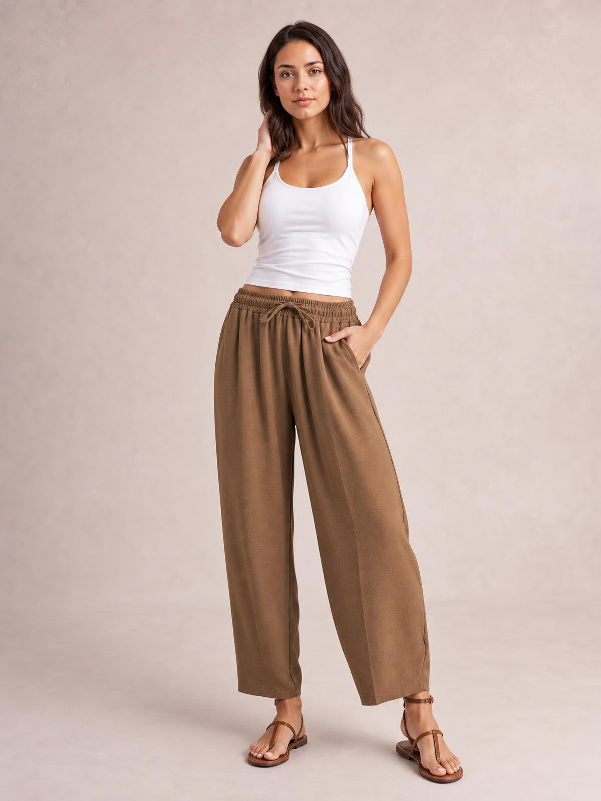 Model wears taupe cropped jogger pants with a drawstring elastic waistband, relaxed wide-leg silhouette, side pockets, and a hand tucked into one pocket.