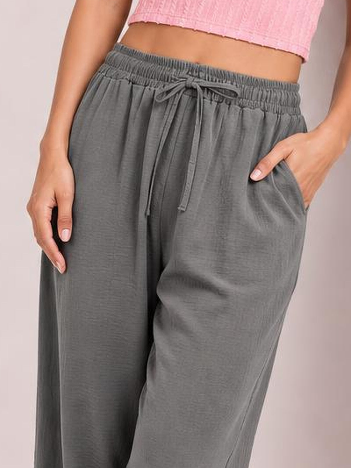 A model wears gray drawstring jogger pants with an elastic waistband, relaxed wide-leg silhouette, side pockets, and hands resting in the pockets.