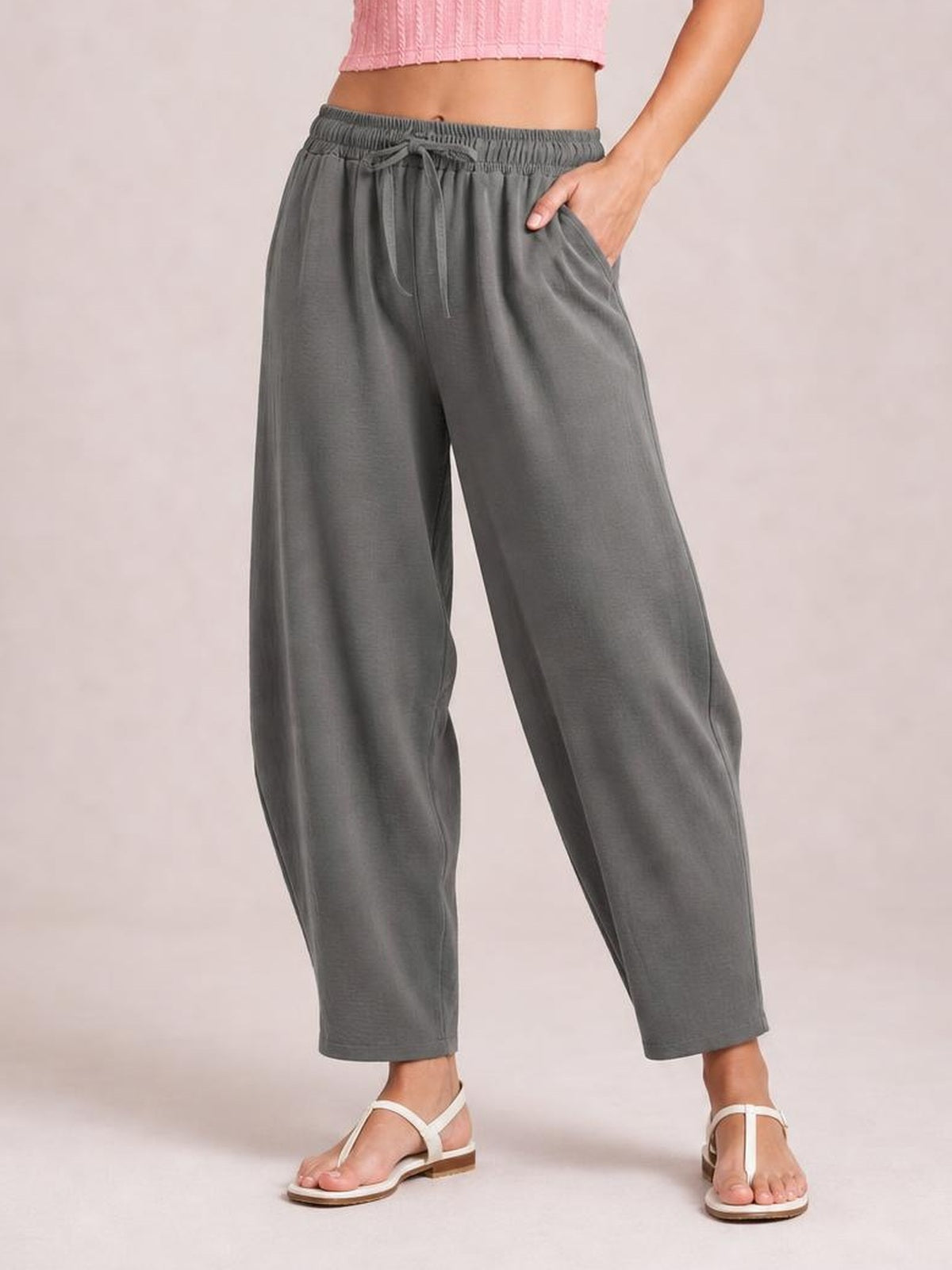 Model wears gray drawstring cropped jogger pants with a relaxed tapered silhouette, elastic waistband, front pockets, and one hand tucked into a pocket.