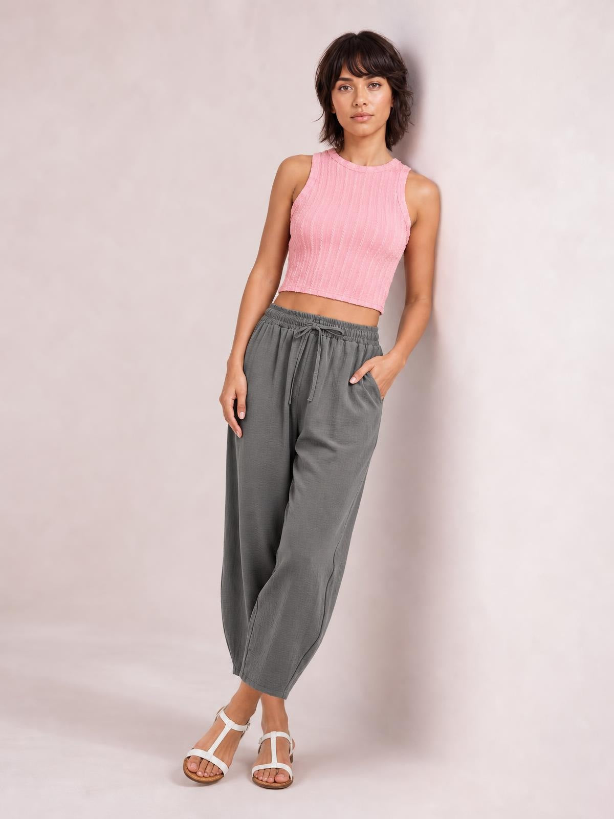 Model poses with one hand in a pocket, wearing gray drawstring cropped jogger pants with an elastic waist, relaxed tapered silhouette, and visible side pockets.