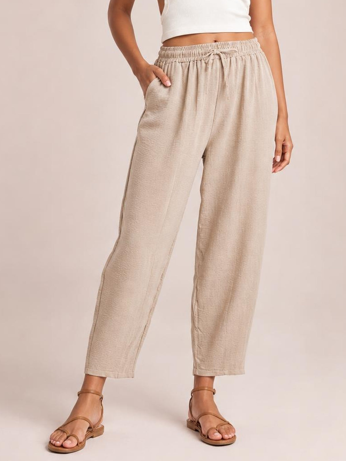 A model wears beige drawstring cropped jogger pants with an elastic waist, relaxed straight-leg silhouette, ankle-length hems, and side pockets.