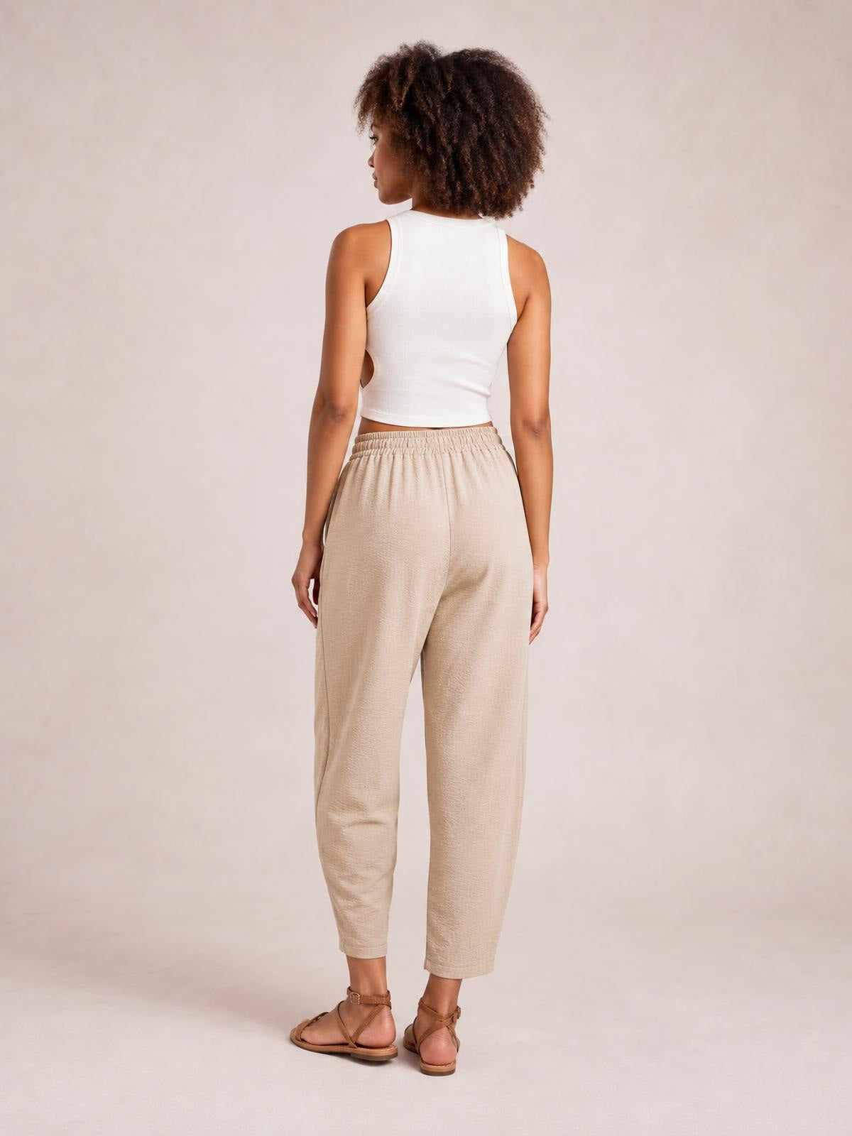 Model shown from behind in beige drawstring cropped jogger pants with an elastic waistband, relaxed tapered silhouette, and ankle-length hems.