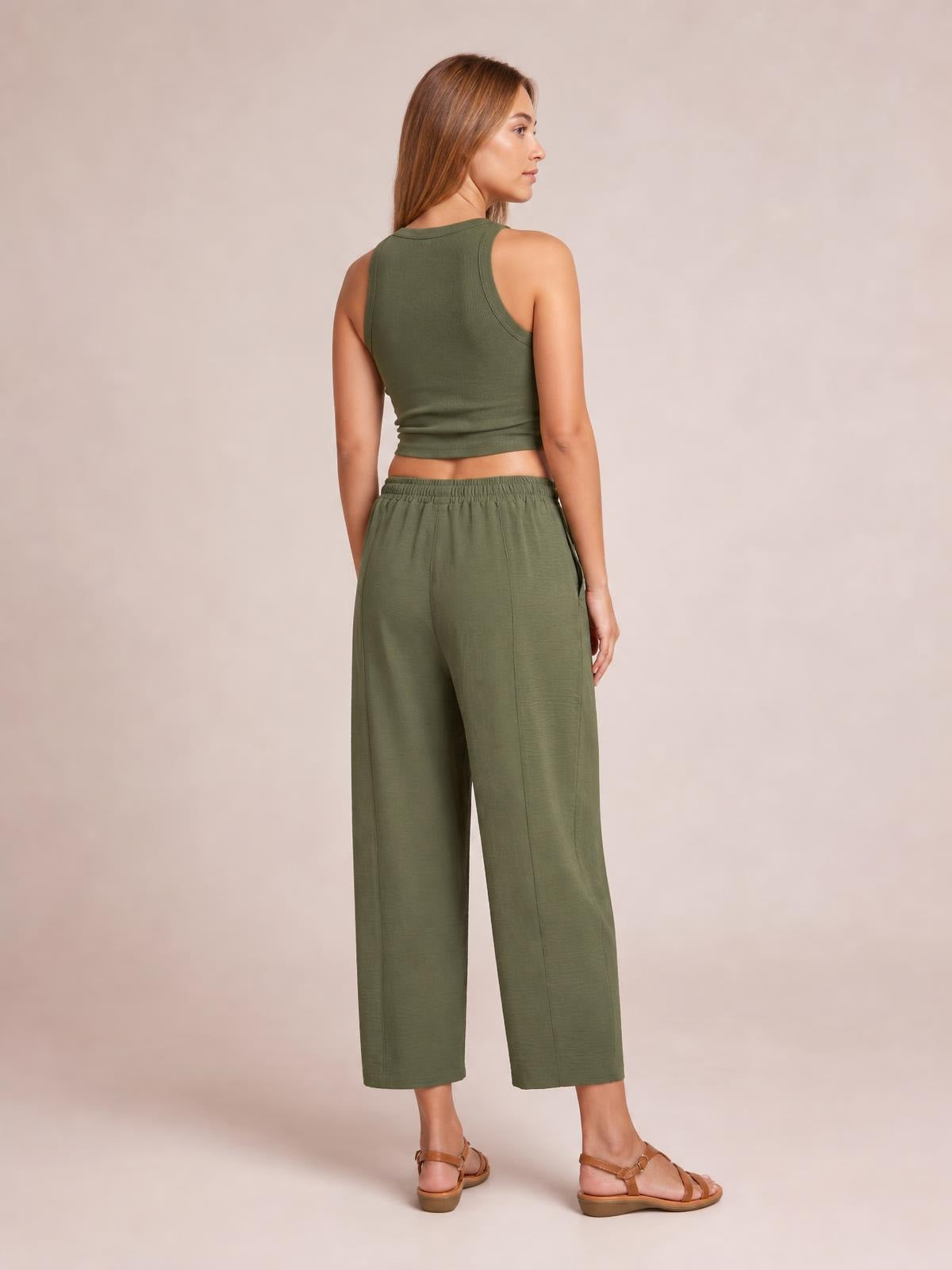 A model poses facing away in olive green cropped jogger pants with an elastic waistband, side pockets, and a relaxed wide-leg silhouette.
