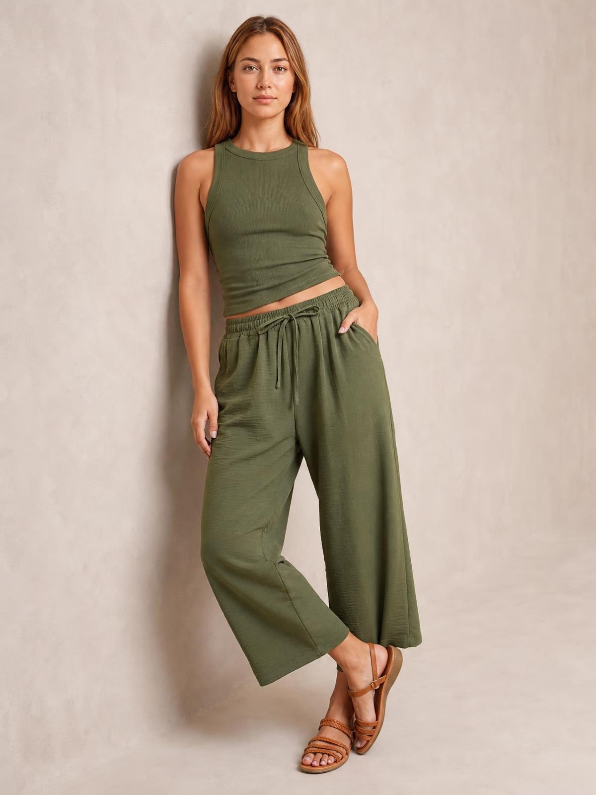 A model poses in olive green cropped jogger pants with a relaxed wide-leg silhouette, elastic drawstring waist, and side pockets, one hand tucked into a pocket.