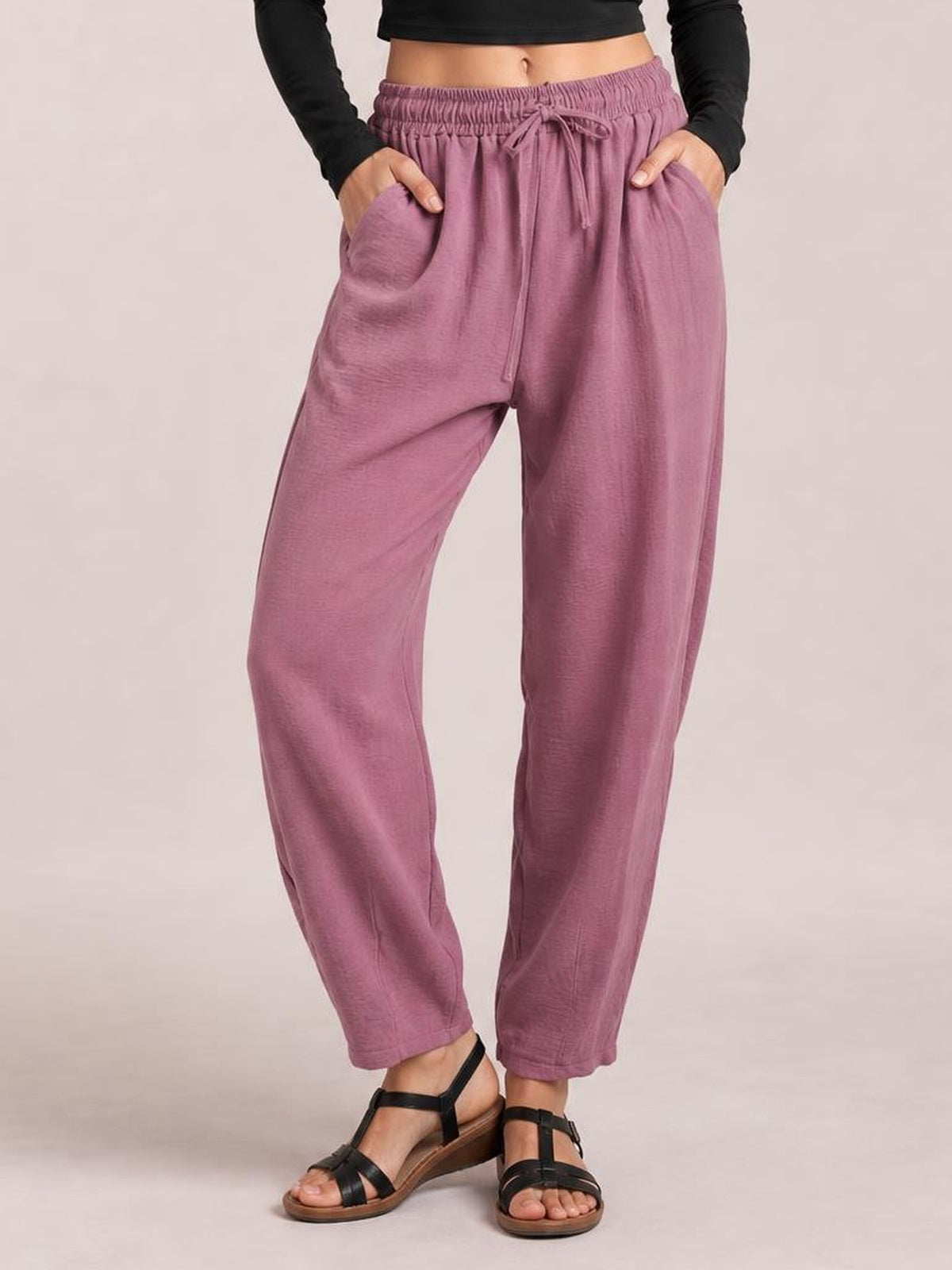 A model poses with hands in the pockets of mauve Drawtising cropped jogger pants featuring a gathered elastic drawstring waist and relaxed tapered silhouette.