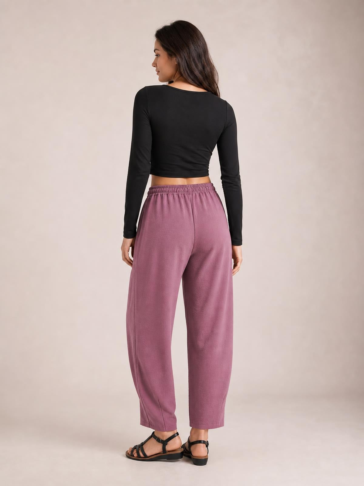 A model poses turned away in mauve cropped jogger pants with an elastic waistband, relaxed silhouette, and ankle-length tapered legs.