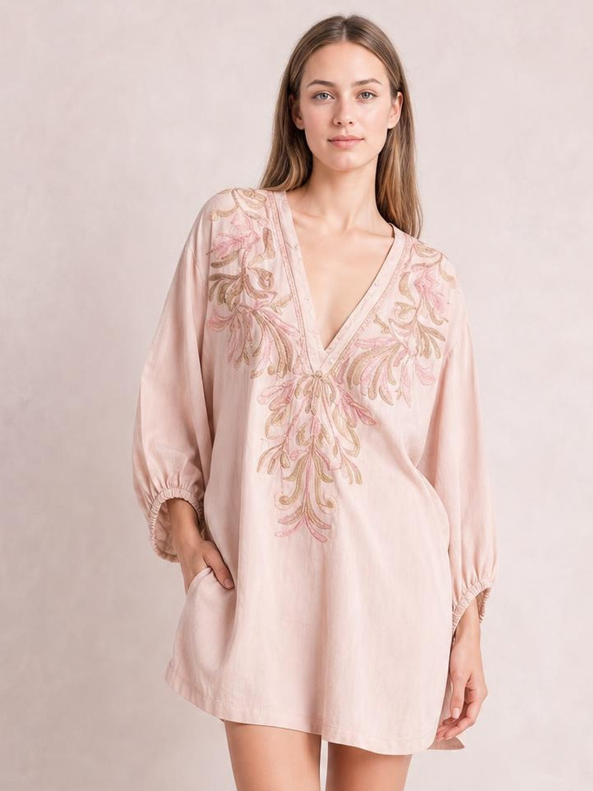 A model poses in a pale pink embroidered V-neck mini dress with a relaxed loose silhouette, long puff sleeves, gathered cuffs, and side pockets.