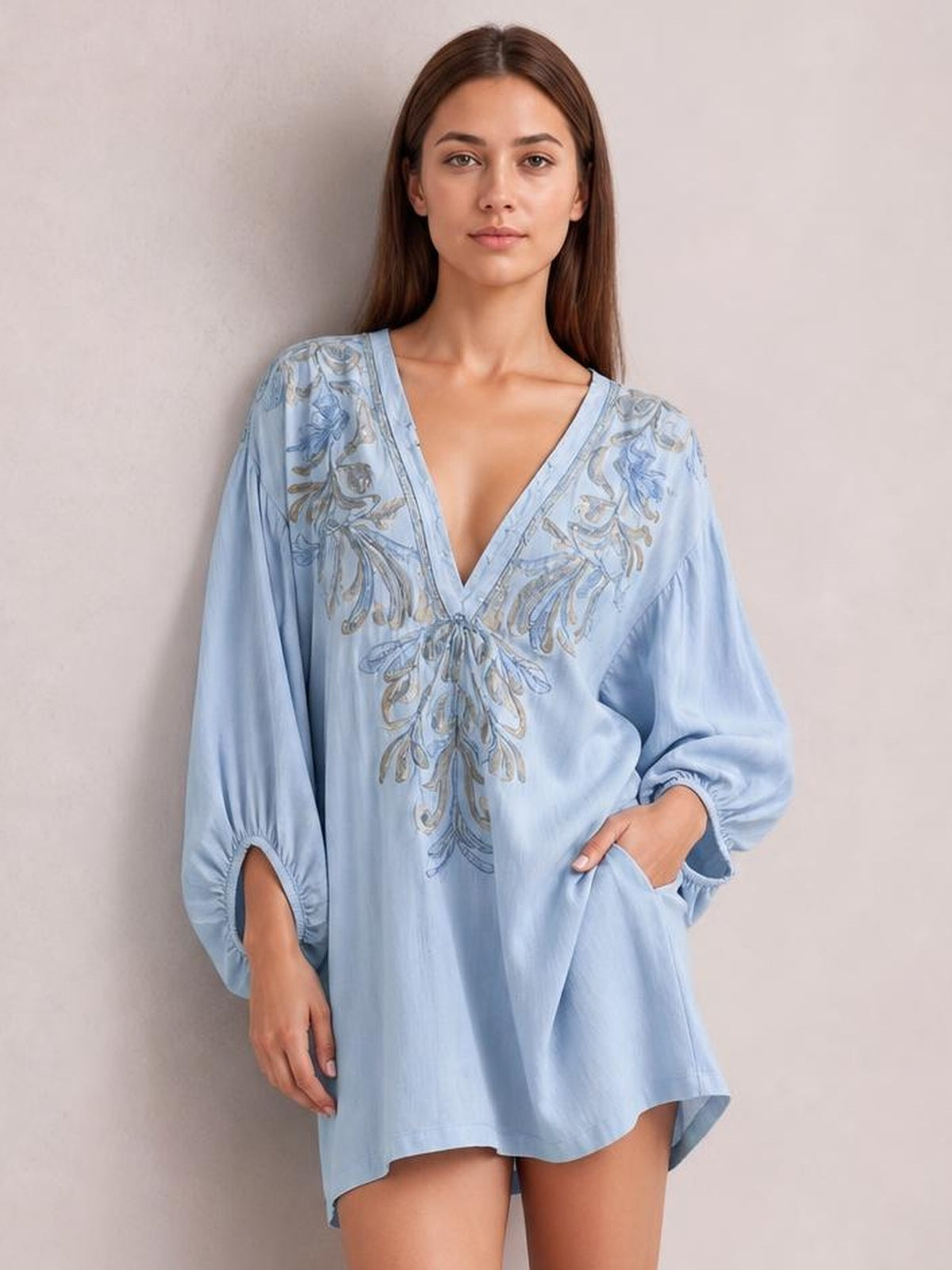 Model wears a light blue embroidered V-neck mini dress with a loose silhouette, long puff sleeves, gathered cuffs, and side pockets.
