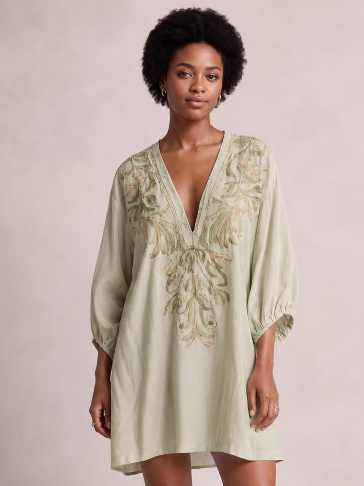 A model stands facing forward in a pale sage embroidered V-neck mini dress with a relaxed loose silhouette and three-quarter sleeves.