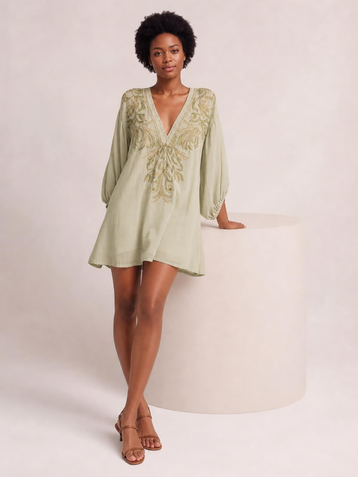 A model stands in a pale sage embroidered V-neck mini dress with long gathered-cuff sleeves, a loose A-line silhouette, and ornate floral detailing.