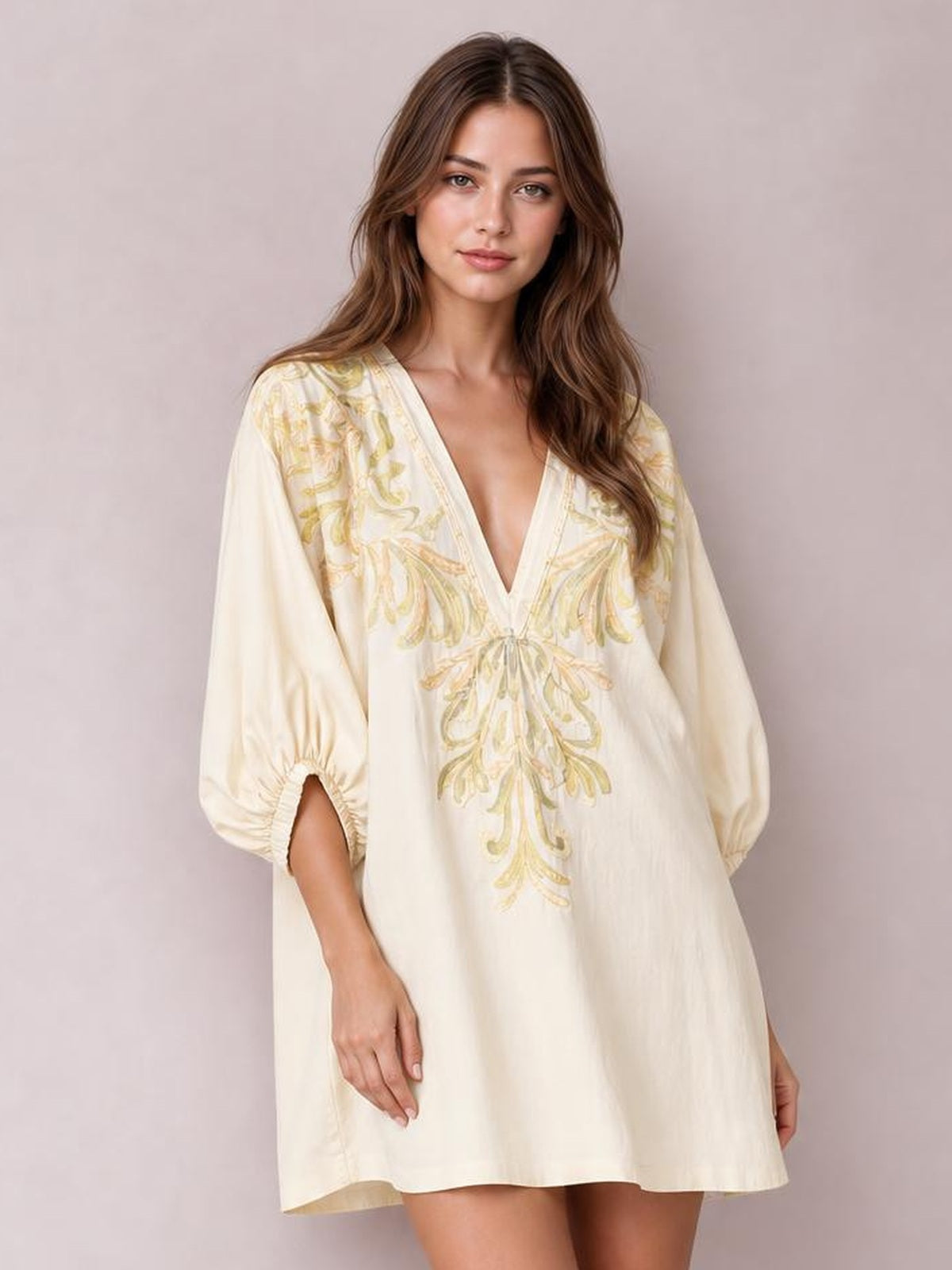 Model wears an ivory embroidered V-neck mini dress with a loose A-line silhouette, long puff sleeves with elastic cuffs, and hands resting near the side pockets.