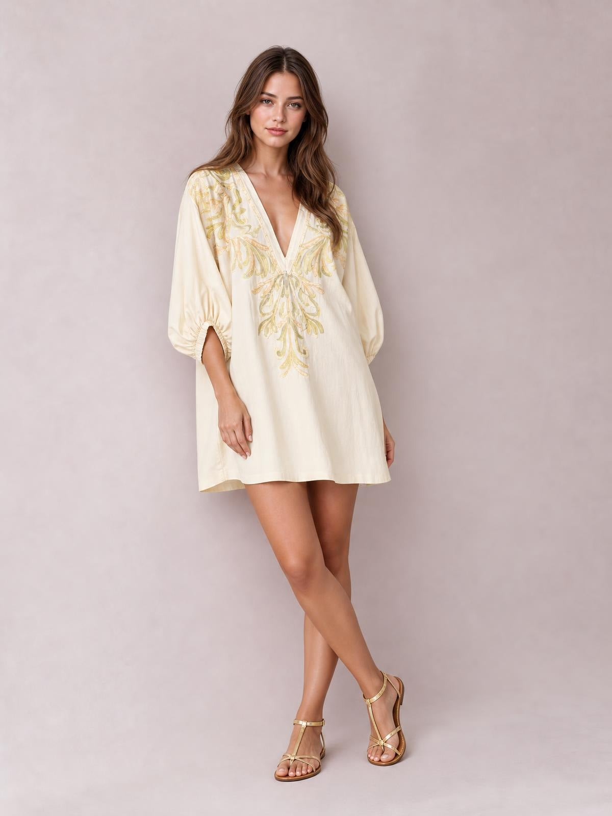A model poses with crossed legs in a cream embroidered V-neck mini dress with a relaxed silhouette, three-quarter balloon sleeves, and side pockets.