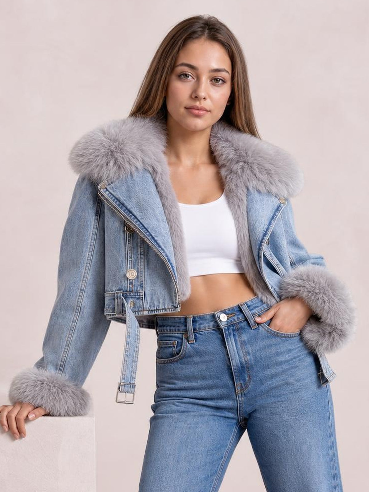 Model poses in a light blue denim jacket with a plush gray faux fur collar and cuffs, cropped silhouette, zip front, belted waist, and angled construction.