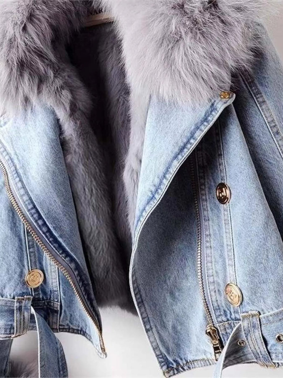 Close-up of a light blue denim jacket with a plush faux fur collar, zip front, gold-tone buttons, lapels, and structured panel stitching.