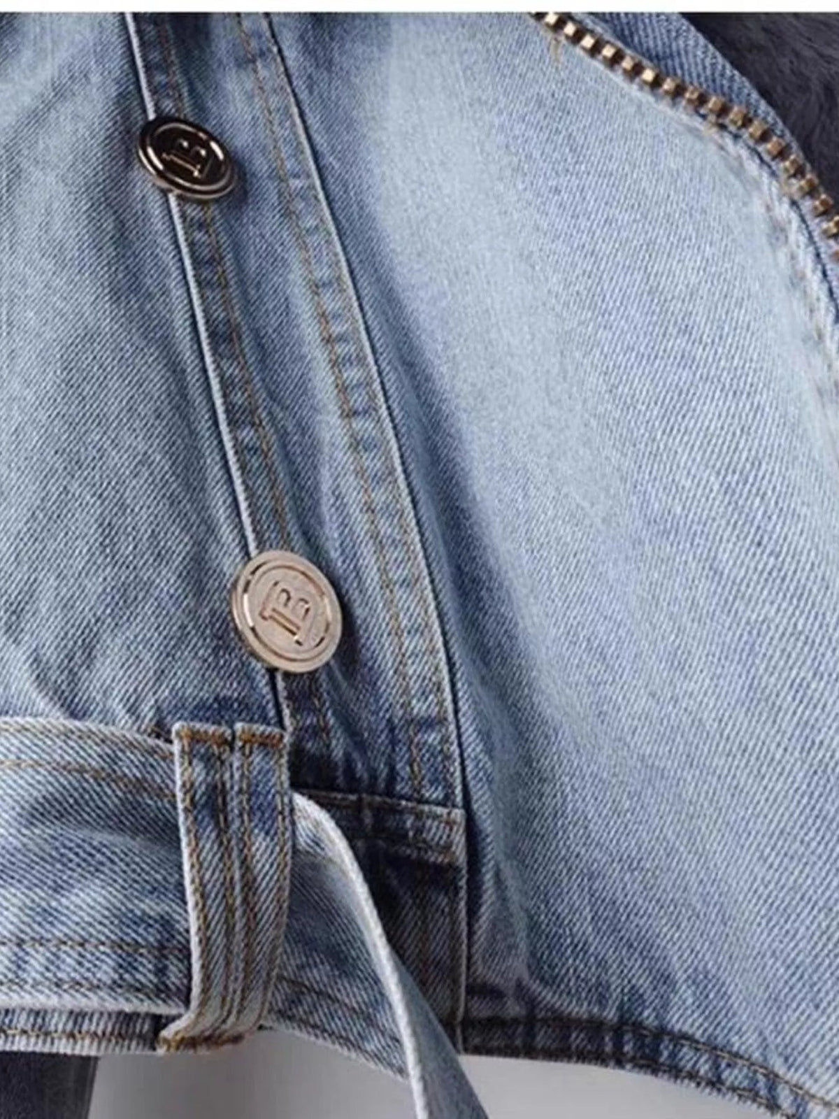 Close-up of a light blue denim jacket showing its faux fur collar, front zipper, metal buttons, and structured stitched panel construction.