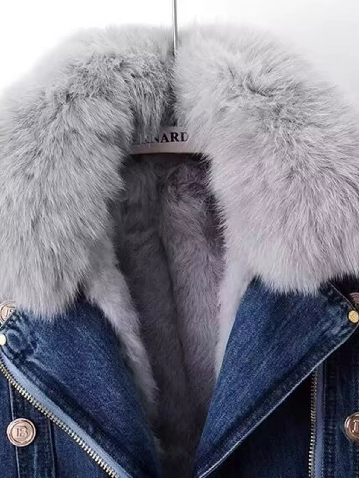 Close-up of a blue denim jacket featuring a plush gray faux fur collar, front zipper, and visible metal snap details.