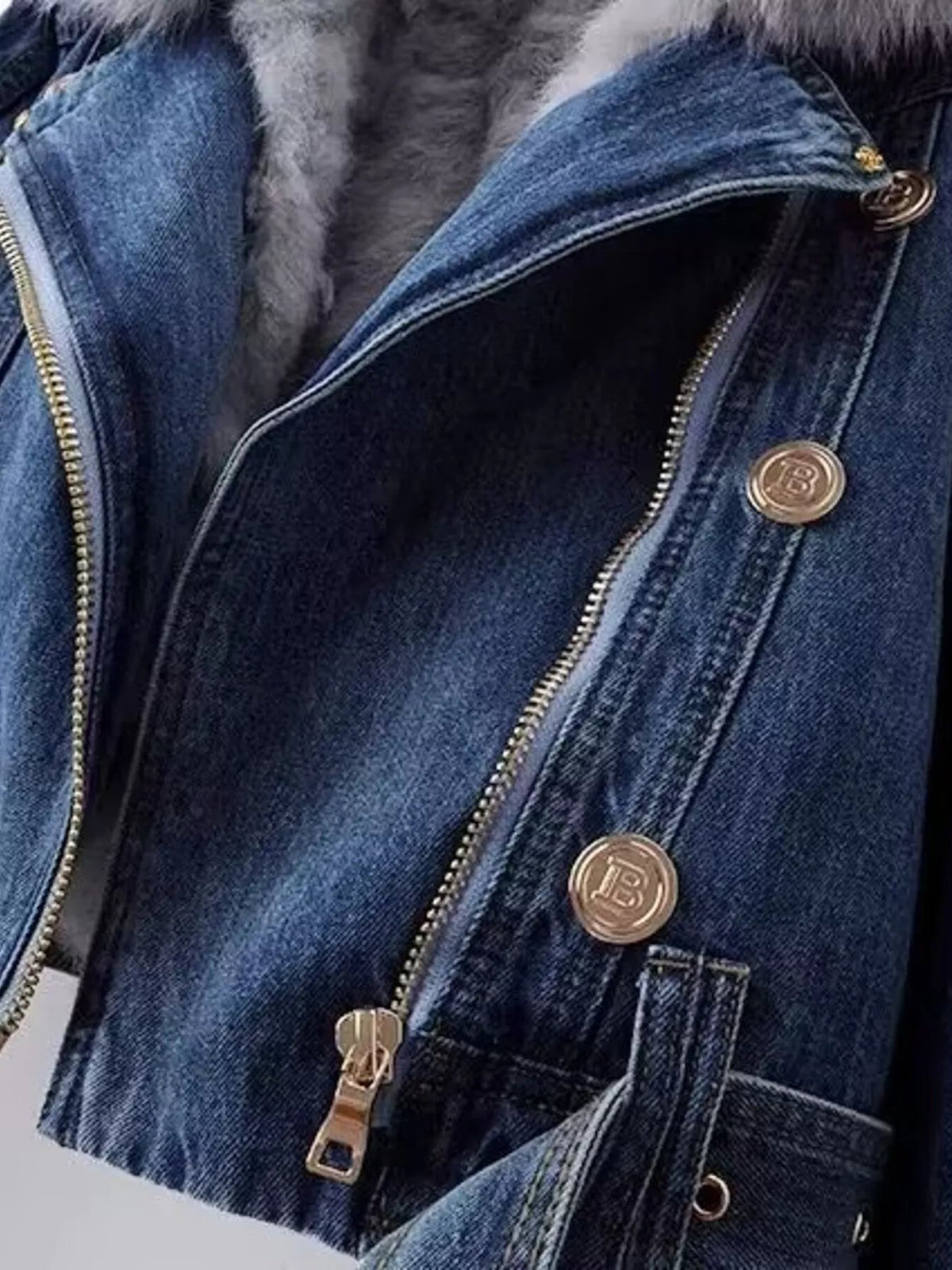 Close-up of a blue denim jacket featuring a plush faux fur collar, asymmetrical zip front, gold-tone buttons, and stitched utility-style pockets.