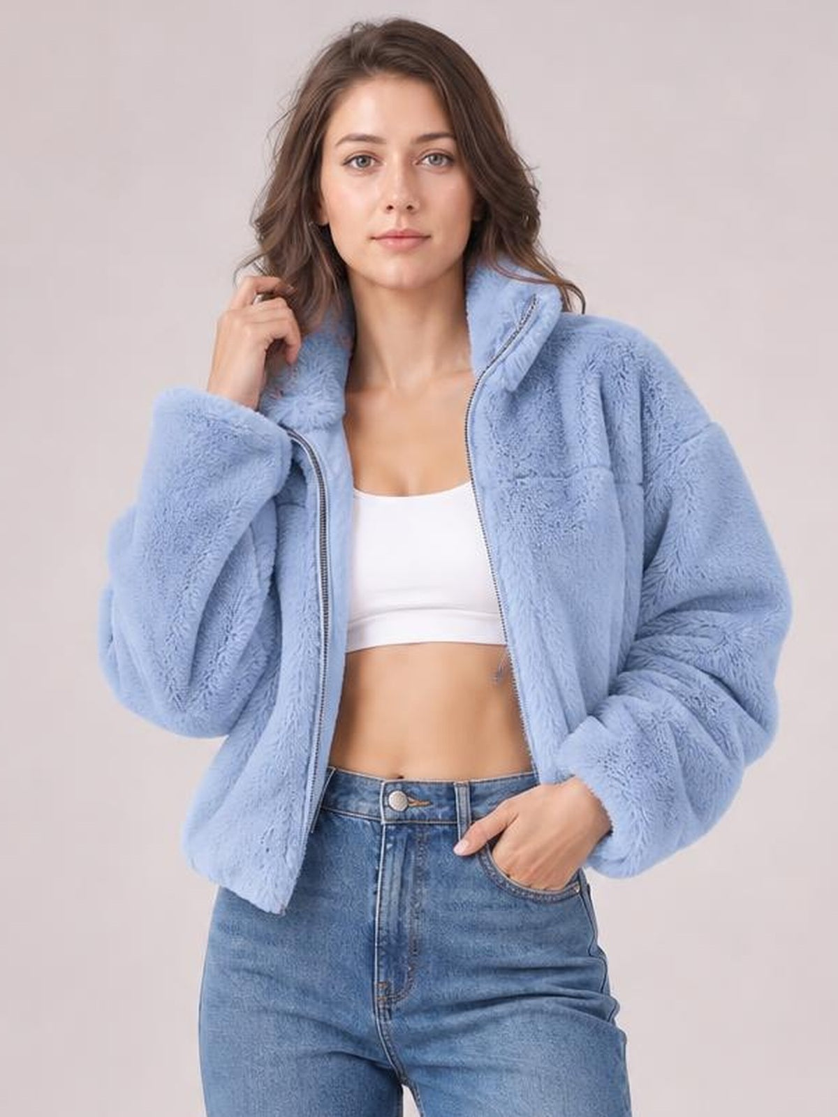 Model poses in a light blue oversized faux fur cropped zip-up jacket, worn open with a plush texture, hood, long sleeves, and relaxed silhouette.