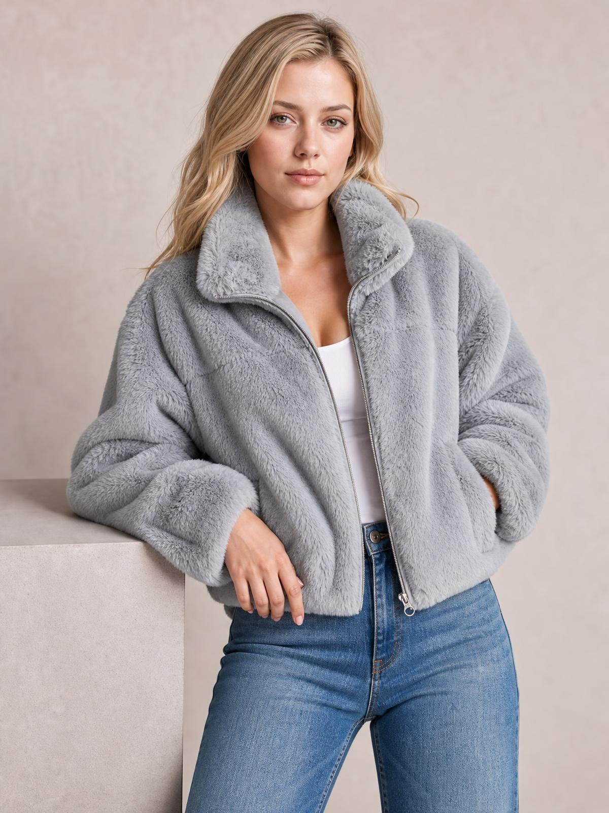 A model poses in a gray faux fur cropped zip-up jacket with an oversized silhouette, plush high collar, long sleeves, and a visible front zipper.