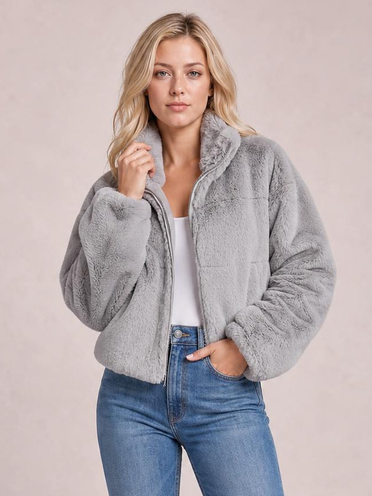 Model poses in a gray faux fur cropped zip-up jacket with an oversized silhouette, plush texture, high collar, and long sleeves.