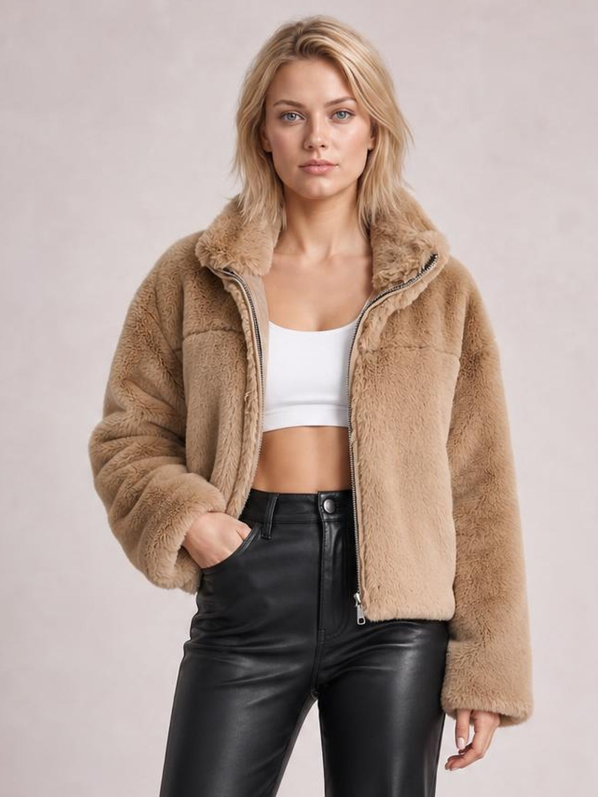 A model wears a tan oversized faux fur cropped zip-up jacket with a plush texture, front zipper, long sleeves, and relaxed silhouette.
