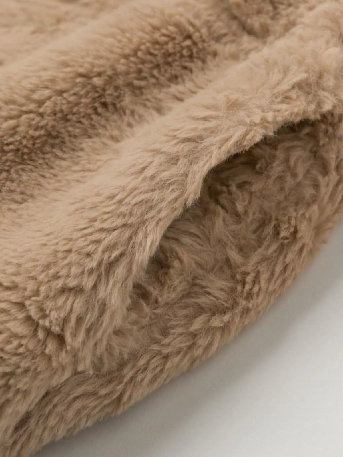 Close-up detail of a taupe faux fur cropped jacket, showing its plush long-pile texture and thick, softly structured construction.