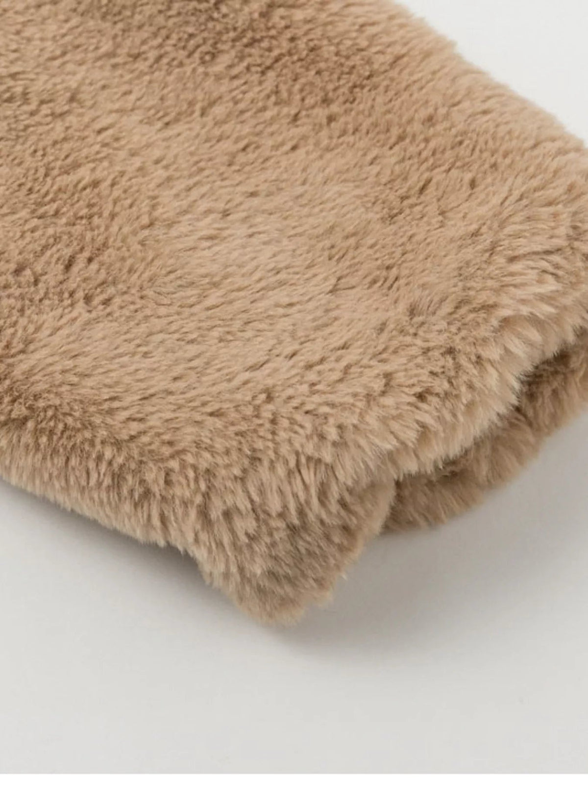 Close-up of a thick beige faux fur jacket showing its soft plush texture, dense pile, and neatly finished cropped hem.