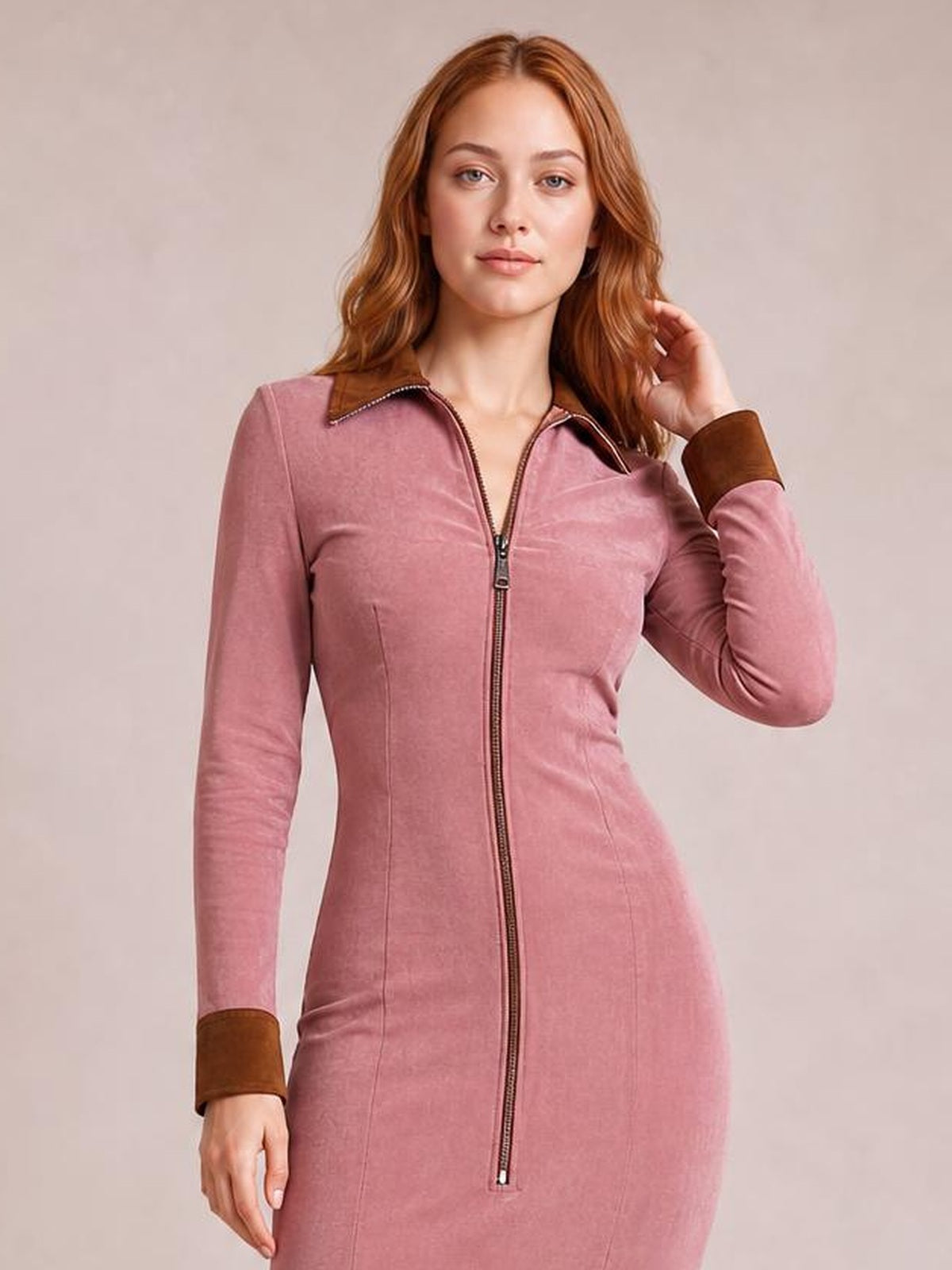 Model poses in a fitted pink midi dress with long sleeves, a full front zipper, contrast brown collar and cuffs, and visible vertical seam detailing.