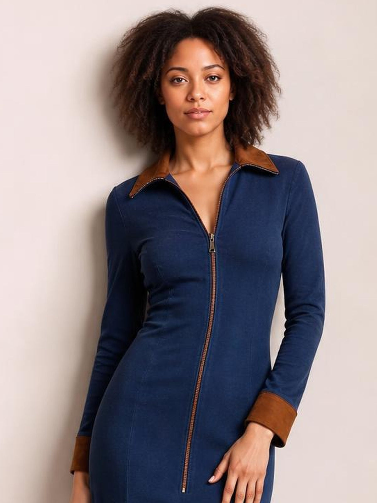 A visible model poses in a fitted navy midi dress with long sleeves, a full front zipper, and contrasting brown collar and rolled cuffs.