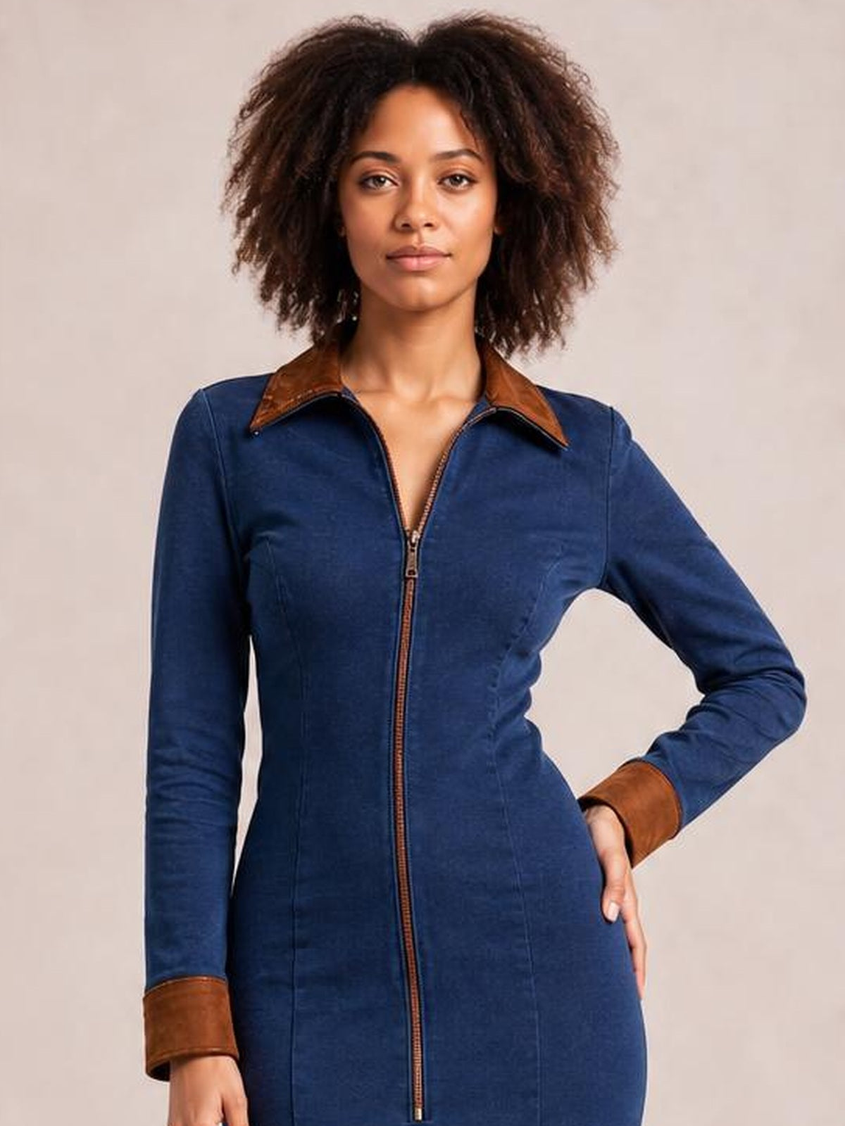 A model poses in a fitted navy zip-front midi dress with long sleeves, a pointed brown collar, contrasting cuffs, and a sleek structured silhouette.
