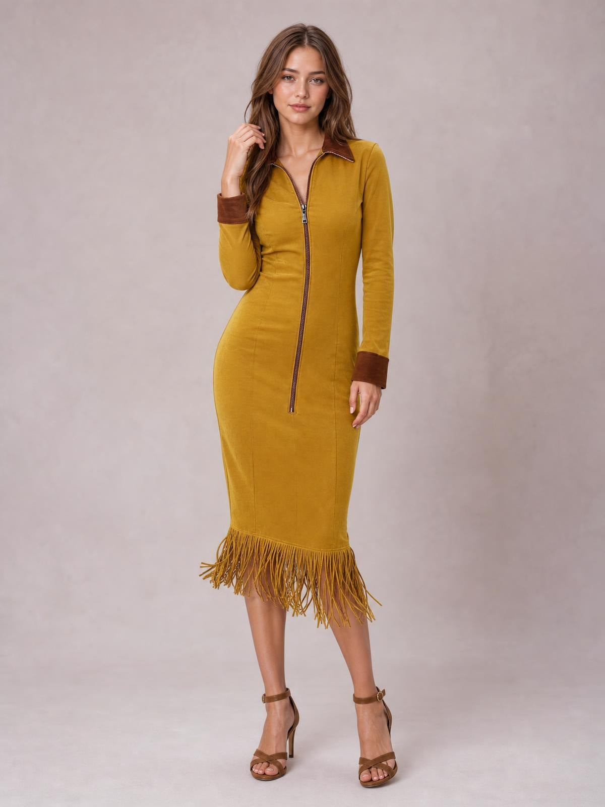 A woman poses with one hand in her hair wearing a mustard-yellow fitted midi dress with a front zipper, long sleeves, contrast collar and cuffs, and a fringe hem.