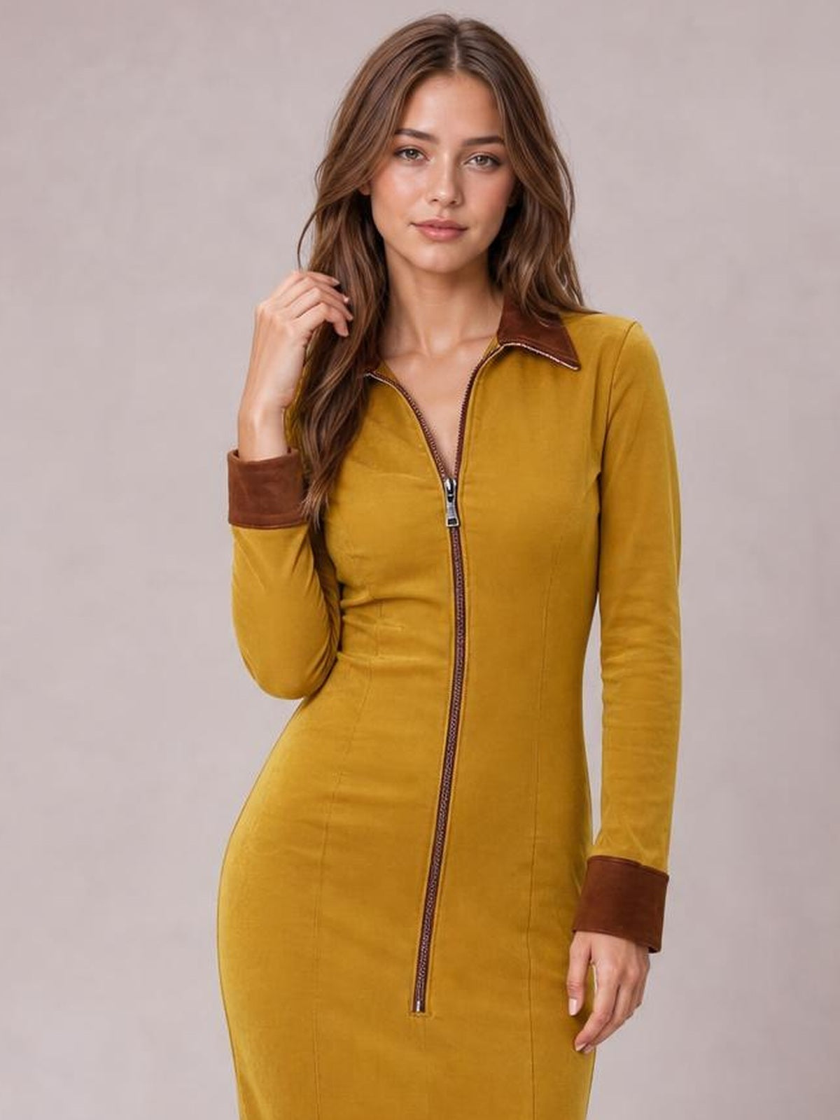 A model poses in a fitted mustard-yellow midi dress with a full-length front zipper, brown contrast collar and cuffs, and long sleeves.