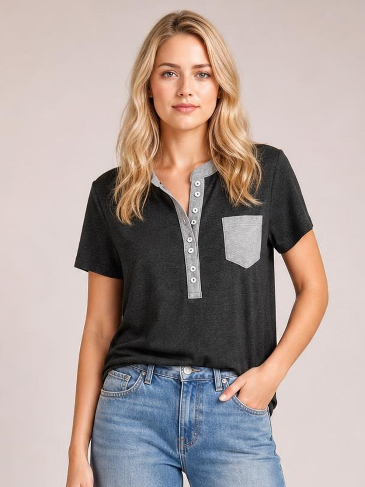 Model wearing a black half button short sleeve T-shirt with gray trim, a button placket, chest pocket, and relaxed silhouette, posing with one hand in her jeans pocket.