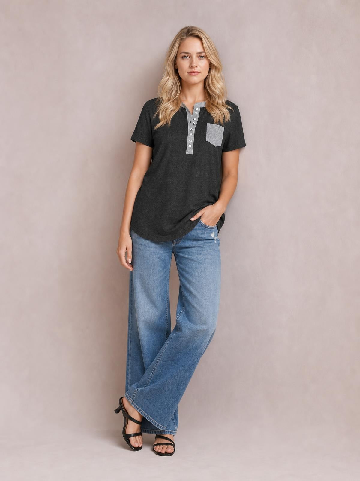 A model poses in a relaxed charcoal short sleeve T-shirt with a half-button placket, gray trim and chest pocket, paired with wide-leg jeans.