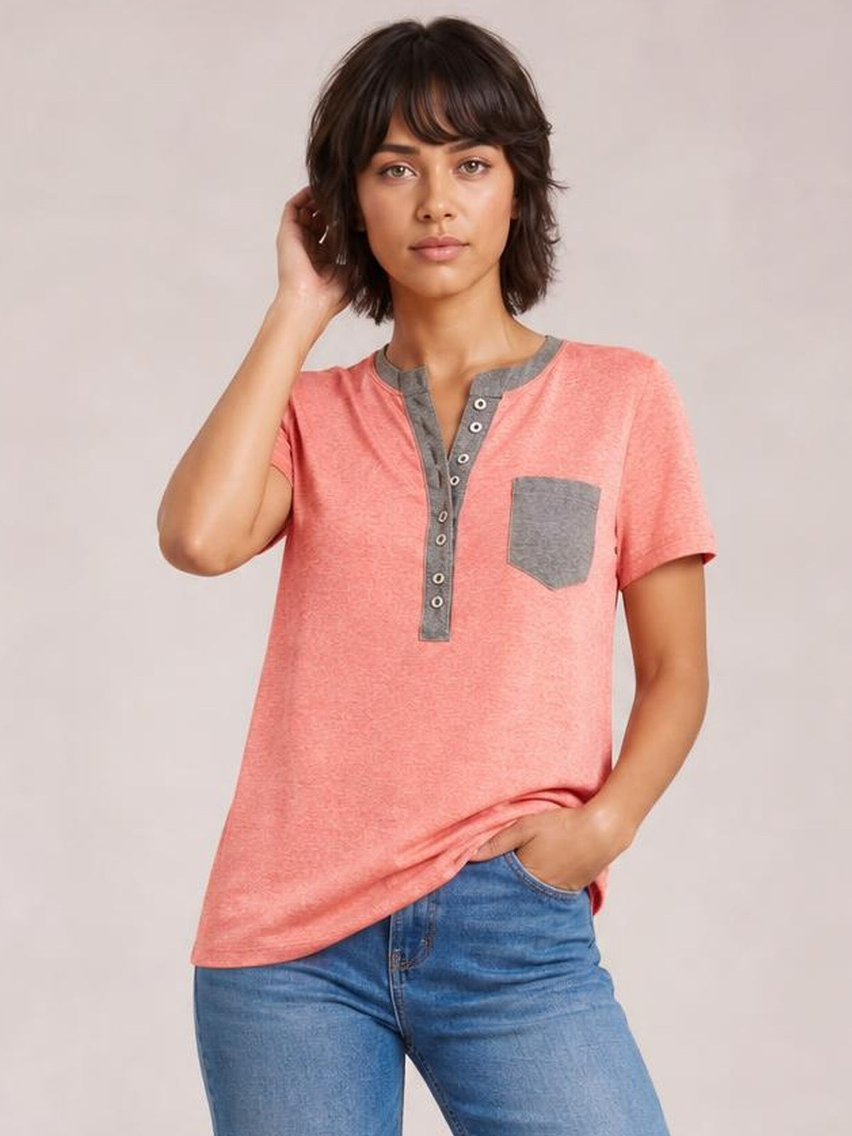 Model wears a coral pink half-button short-sleeve T-shirt with a gray button placket and chest pocket in a relaxed, straight silhouette.