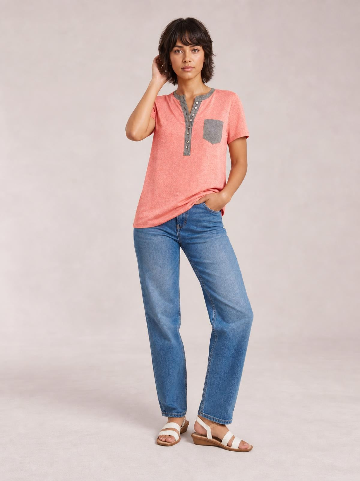 Model poses in a coral pink short sleeve T-shirt with a gray half-button placket and chest pocket, featuring a relaxed straight silhouette.