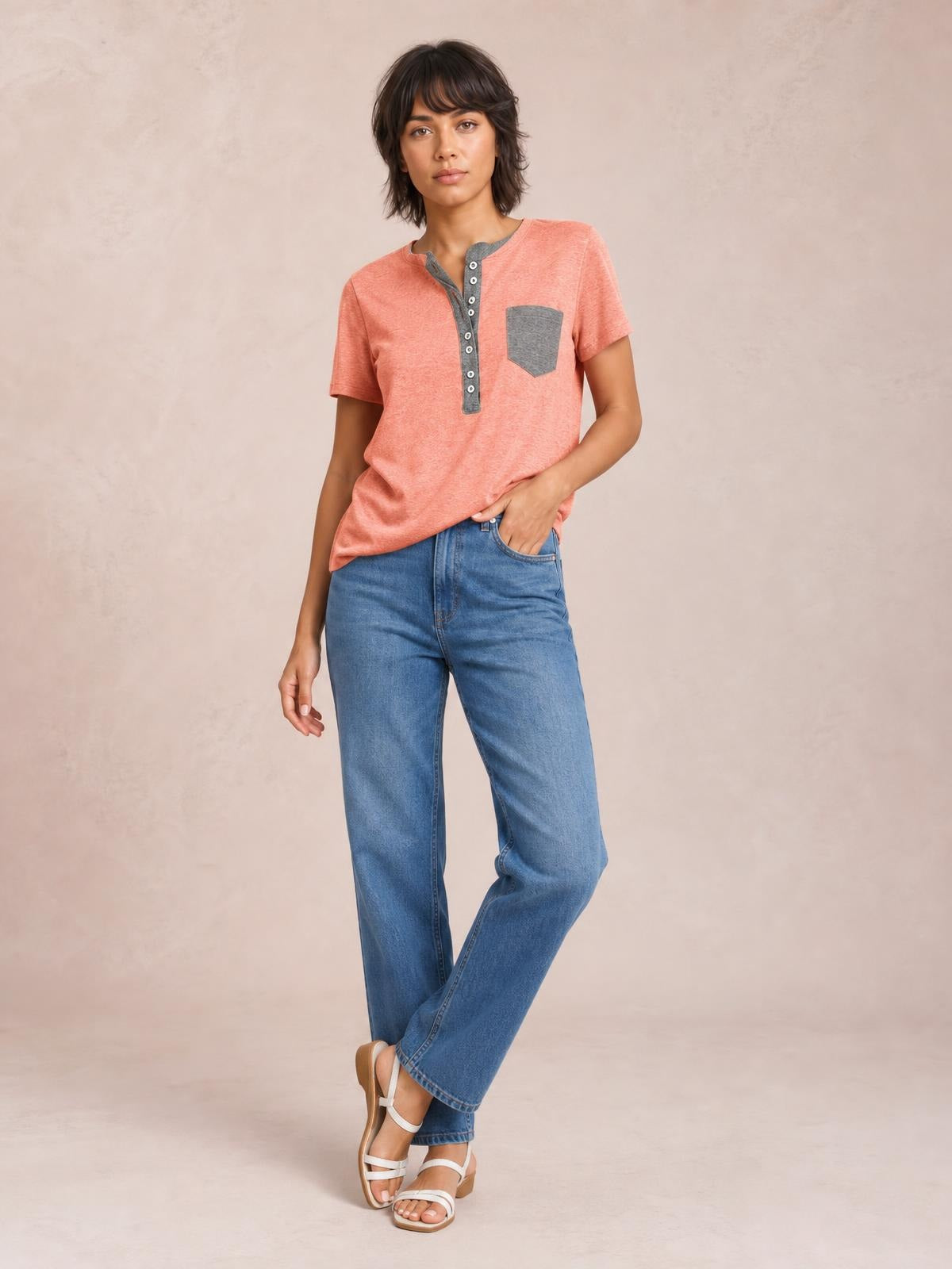 Model poses in a coral short-sleeve T-shirt with a gray half-button placket and chest pocket, featuring a relaxed silhouette and curved hem.